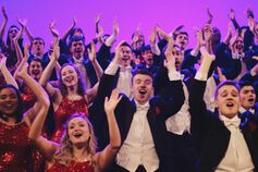 Members of the Singing Hoosiers sing and clap on a purple-lit stage.